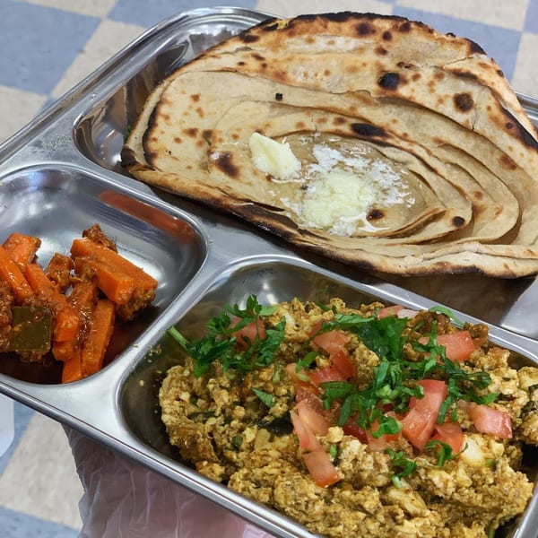 Indian breakfast platter with paratha, paneer bhurji, and carrot pickle in a metal tray.