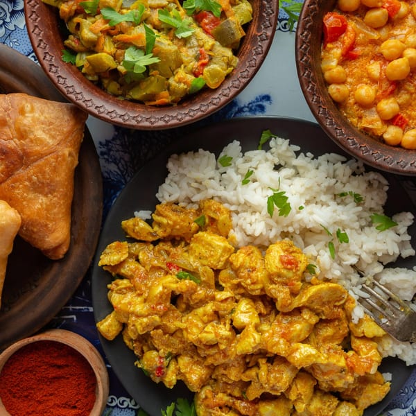 Overhead view of Indian dishes: chicken curry with rice, chickpea curry, vegetable curry, and samosas.