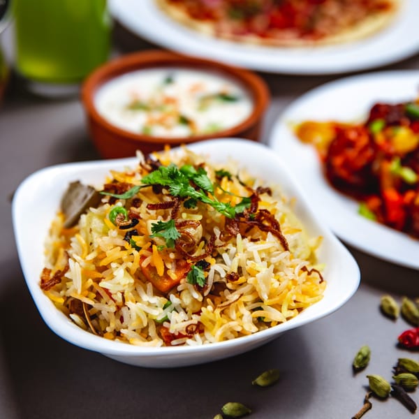 A white bowl of colorful Indian biryani rice with cilantro, fried onions, and spices.