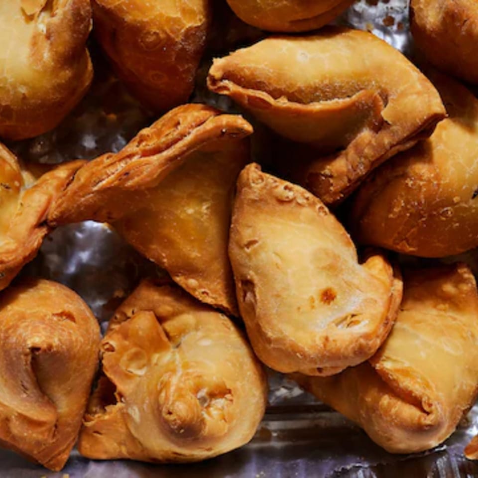 Assorted golden-brown fried pastries, including triangular and crescent-shaped pieces, piled together.