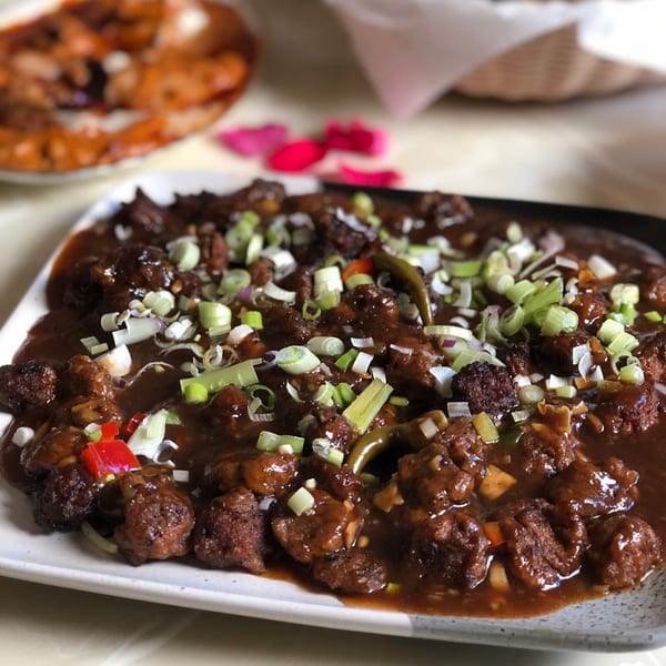 Chit Chaat Cafe's Indian dish of dark brown Manchurian balls in gravy, garnished with green onions.