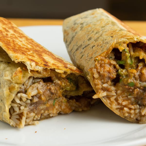 Two halves of a golden-brown Indian burrito, revealing a filling of rice and curry on a white plate.