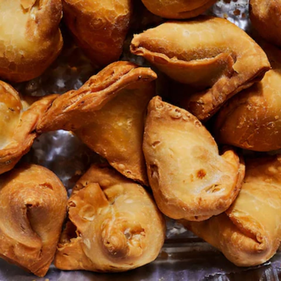 Assortment of golden-brown fried pastries, including triangular and crescent-shaped pieces, piled on a serving tray.