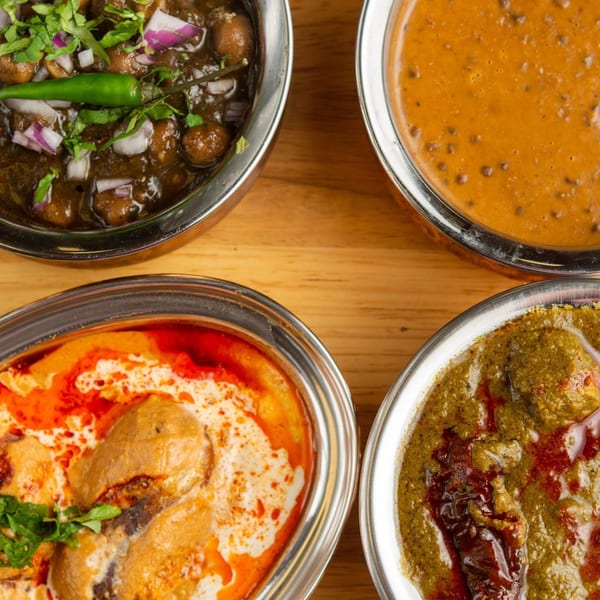 Four bowls of colorful Indian dishes, including chana masala, dal makhani, butter chicken, and saag paneer.