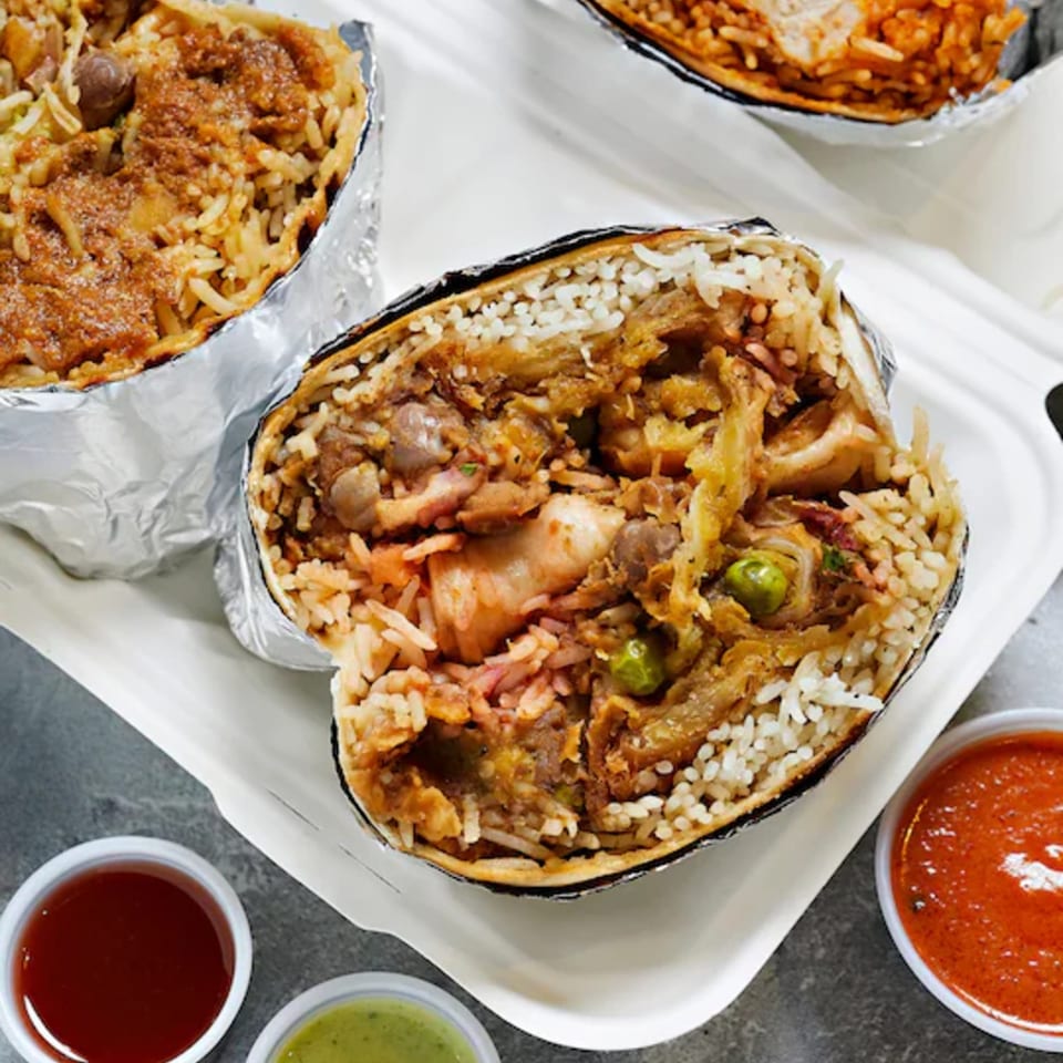 Open foil trays filled with spiced rice, grilled chicken, vegetables, and meat, served with red and green sauces.