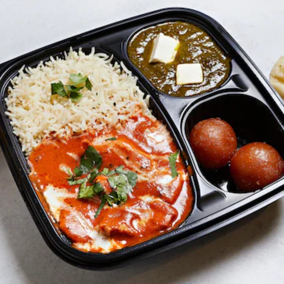 Indian takeout meal with basmati rice, creamy tomato curry, lentil dal topped with paneer, and two gulab jamuns.